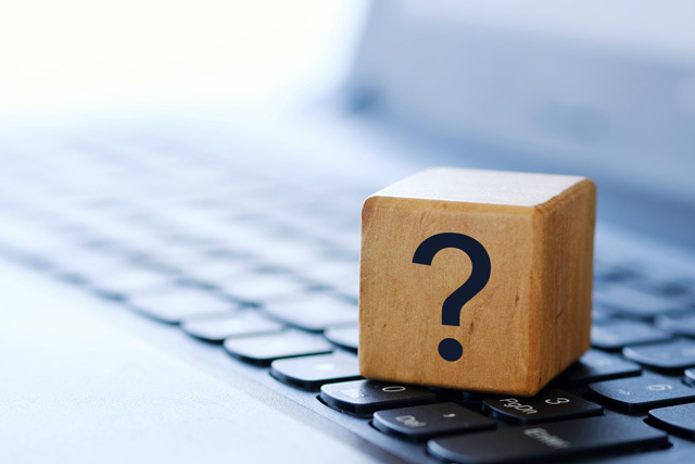 Ein Holzwürfel mit einem Fragezeichen liegt auf der Tastatur eines Laptops. Das Symbolbild soll die FAQ zur digitalen Baugenehmigung darstellen.